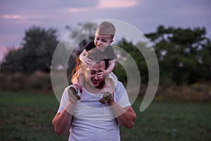 Diversity father with beard carrying son on shoulders shares tender moment in twilight lit field