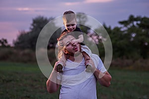 Diversity father with beard carrying son on shoulders shares tender moment in twilight lit field