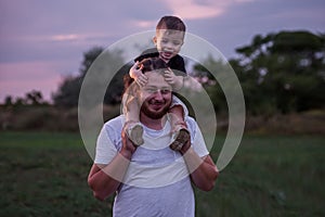 Diversity father with beard carrying son on shoulders shares tender moment in twilight lit field