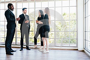 Diversity group of businesspeople strictly dressed in the suits standing meeting by office window.