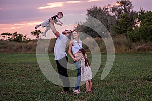 Diversity happy family plays in field at sunset. Young father lifting toddler high in the air