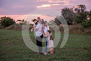 Diversity happy family plays in field at sunset. Young father lifting toddler high in the air