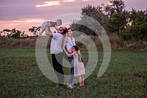 Diversity happy family plays in field at sunset. Young father lifting toddler high in the air