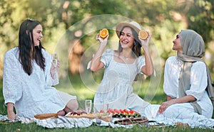 Diversity, Islamic and friends on a fruit picnic on grass in nature enjoying orange, watermelon and fun jokes. Muslim