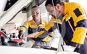 Diversity mechanic teamwork, an Indian man and an African woman in yellow and blue uniforms. A man inspects the car engine.