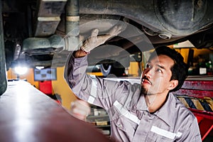 Diversity mechanic teamwork, a Japanese mechanic repairman in a grey uniform inspects the car bottom problems of a lifted car.