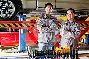 Diversity mechanic teamwork, a Thai and Japanese man in blue uniforms standing and arm crossed in front of the lifted car.