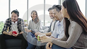 Diversity of young people group team holding coffee cups and discussing something with smile while sitting on the couch at office