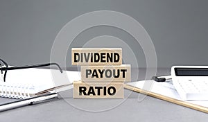 DIVIDEND PAYOUT RATIO text on wooden block with notebook,chart and calculator, grey background