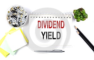 DIVIDEND YIELD text on notebook with office supplies on white background