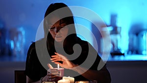 Divination by candlelight, young modern woman is sitting alone at night and looking in flame of candle