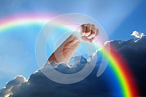 Divine hand god holding rainbow in fist out of clouds