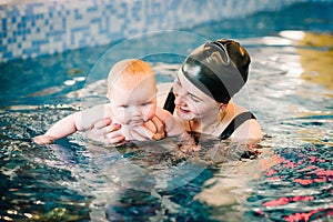 Diving baby in the paddling pool. Young mother, swimming instructor and happy little girl in pool. Learn infant child to swim.