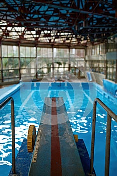 Diving board at empty swimming pool with reflections of light in water