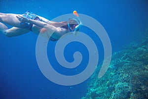Diving girl underwater with coral reef. Snorkel in full face mask.