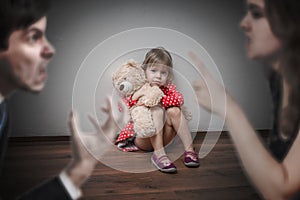 Divorce concept. Sad child is sitting at floor when parents argue.