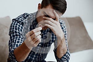 Divorce concept. Sad lonely man holding engagement ring sitting at home. Depression after a divorce. Selective focus.