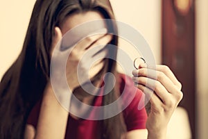 Divorce concept. Sad lonely woman holding engagement ring sitting at interior home close-up. Selective focus.