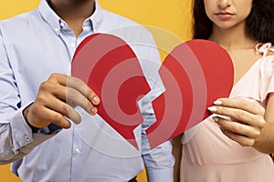 Divorce, separation concept. Unrecognizable indian couple holding halves of broken heart over yellow background