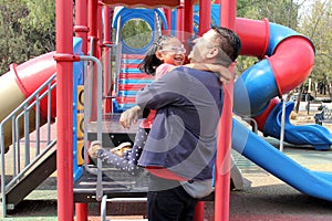 Divorced dad plays with his brunette latina daughter in playground park spins and hugs spend fun time photo
