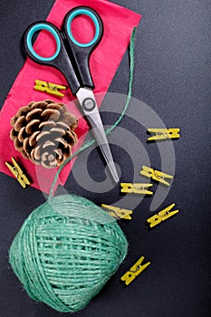 DIY background concept DIY tools scissors, green wood clip, string, pine corn and red paper on black background