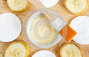 Diy banana mask face cream in the small white bowl, make-up brush, cotton pads and banana slices.