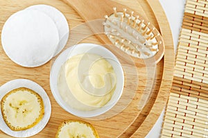 Diy banana mask face cream in the small white bowl, wooden hair brush, cotton pads and banana slices.