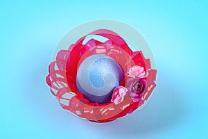 Diy Easter egg basket made of red plastic cup decorated with artificial flowers on blue background