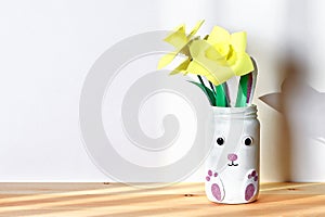 DIY Easter vase bunny with narcissus, daffodils from glass jar, felt, eyes on white wall background