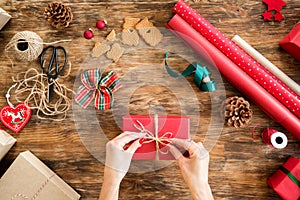 DIY Gift Wrapping. Woman wrapping beautiful red christmas gifts on rustic wooden table. Overhead point of view.