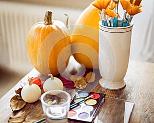 DIY Halloween concept. Art and craft, decorating Halloween pumpkins. Color pallete, paintbrush and pumpkins on a table.