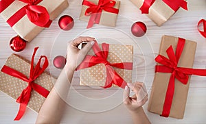 DIY hobby concept. Woman& x27;s hands wrapping christmas holiday handmade gift box in paper with red ribbon, top view