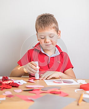 DIY holiday card with red paper heart, symbol of love. Kid boy makes Mother`s Day, Valentine`s Day, greeting card. Hobby, childr