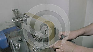 Diy man looking at metal knife and grinding it on abrasive machine, partial view