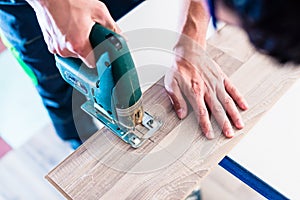 DIY worker cutting wooden panel with jig saw photo