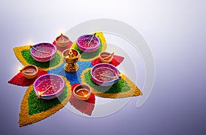 Diya lamps lit on colorful rangoli with copy space