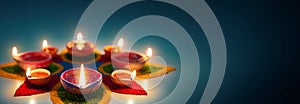 Diya oil lamps lit on colorful rangoli with copy space