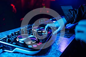 DJ console for mixing music with hands and with blurred people dancing at a night club party