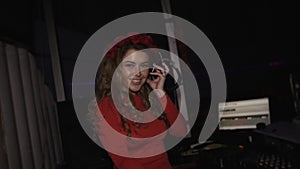 Dj girl in red dress with rim on head touch face by hand at turntable in club