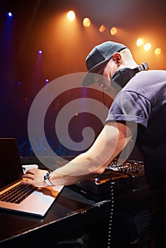 DJ, man and laptop at nightclub for concert with spotlights, turntables and live music show. Professional person with