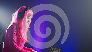 Dj in pink hair mixing electronic sound using mixer console