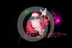 Dj Santa Claus at Christmas with glasses and snow mix on New Year`s Eve event in the rays of light