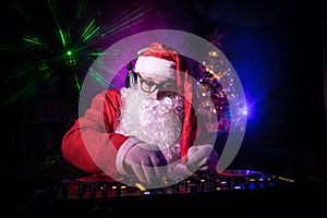 Dj Santa Claus at Christmas with glasses and snow mix on New Year`s Eve event in the rays of light