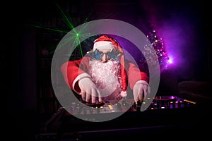 Dj Santa Claus at Christmas with glasses and snow mix on New Year`s Eve event in the rays of light