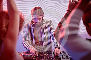 DJ by turntable in neon lights with dancing crowd in nightclub