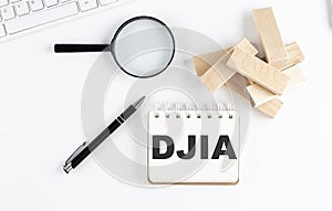 DJIA word written on notebook with block magnifier and pen , business concept