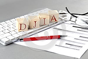 DJIA written on a wooden cube on the keyboard with chart on grey background
