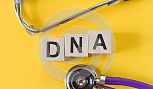 DNA inscription on wooden cubes isolated on yellow background, medicine concept. A stethoscope is on the table next to it