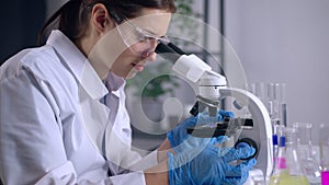 DNA research in modern laboratory, woman is viewing sample under microscope