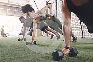 Do as many reps as you can. a fitness group using dumbbells while doing push-ups at the gym.